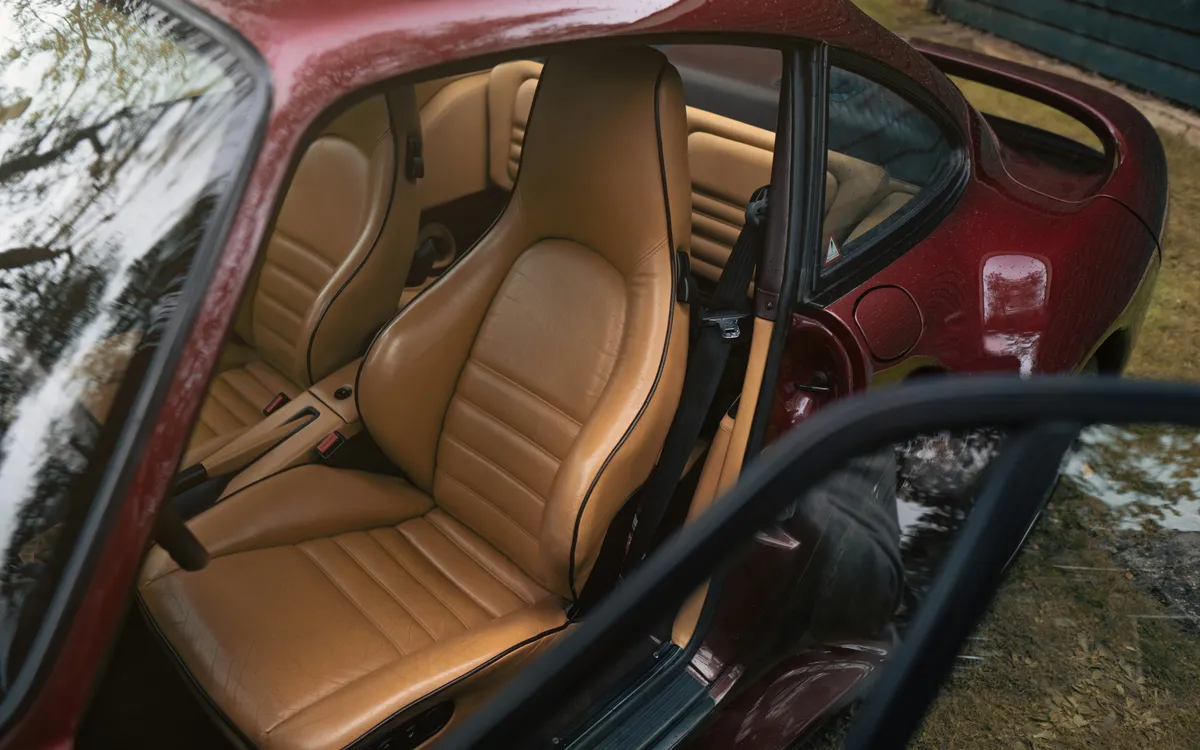 Tan leather seats through the open door of a red car