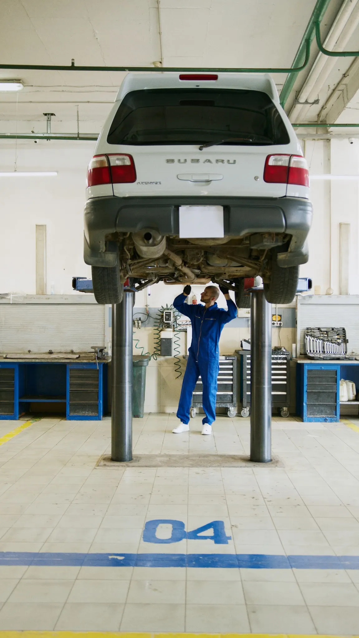 A mechanic inspecting the underside of an older Subaru Forester on a workshop lift